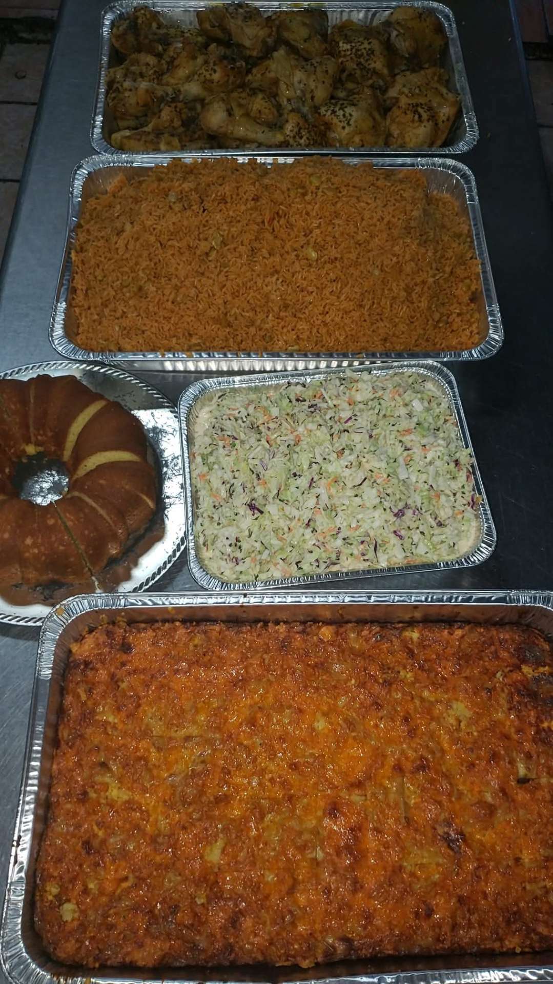 Catering trays of baked chicken, peas and rice, coleslaw, baked macaroni and guava cake